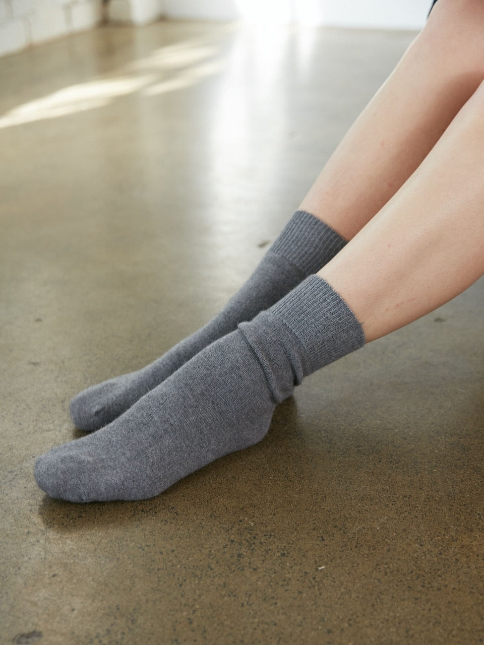 A woman's legs are sitting on the floor wearing general sleep's Bed Socks – Moon.