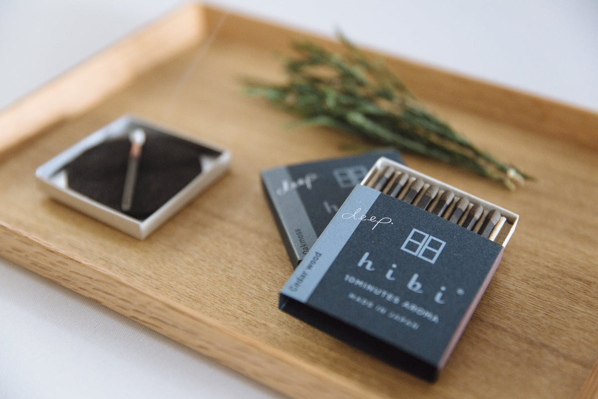 A hibi wooden tray with a Match Box Incense – Deep Scent Gift Box and a sprig of rosemary.