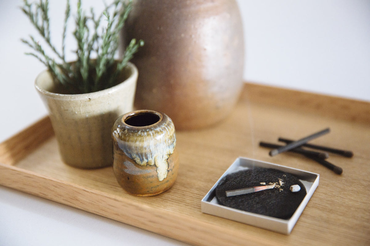 A tray with a hibi Match Box Incense Deep – Oak Moss and a plant on it.