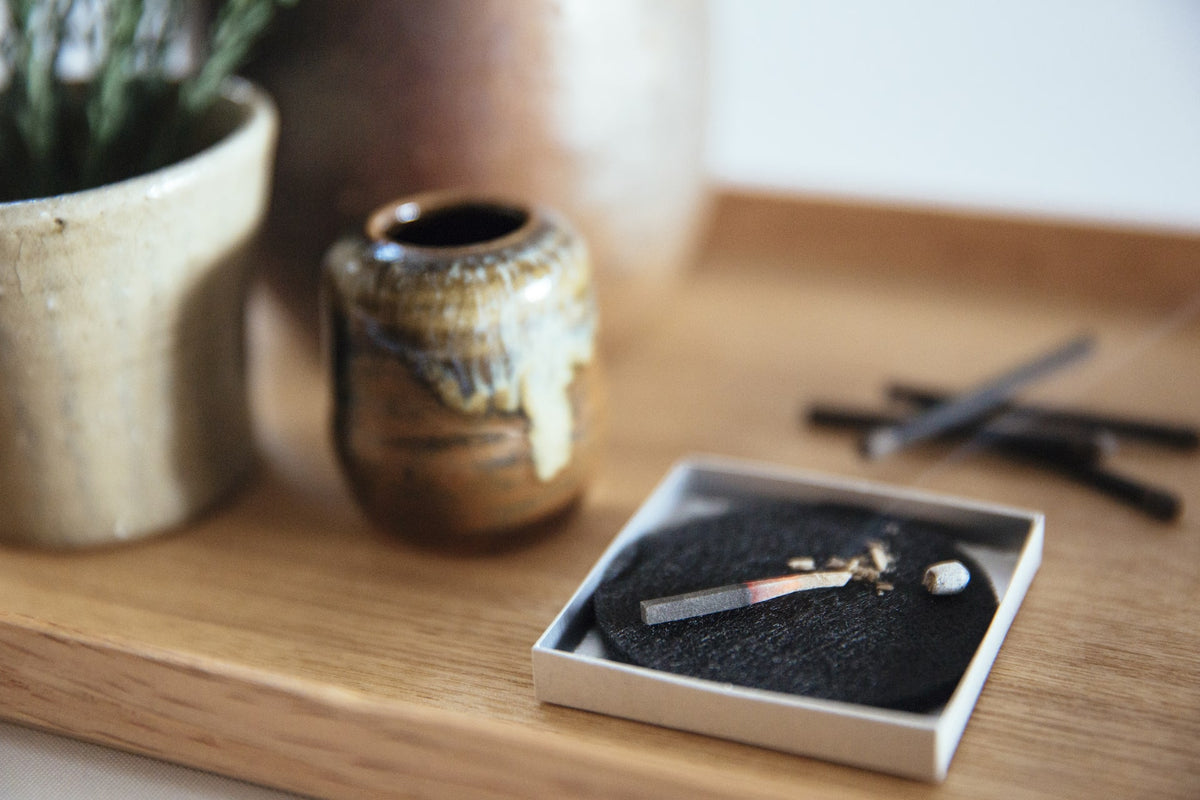 A hibi wooden tray with a Match Box Incense Deep – Ambergris candle and a vase on it.