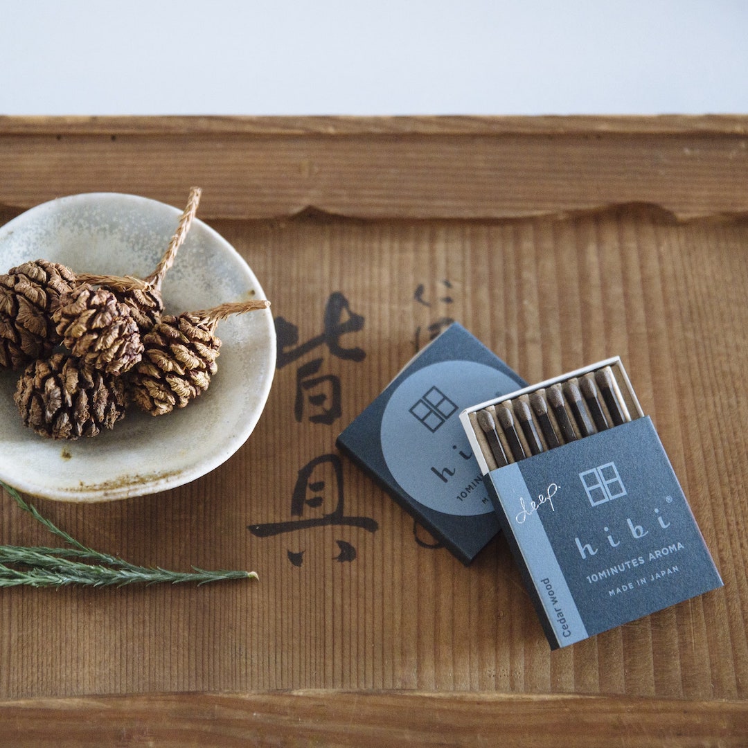 hibi Match Box Incense Deep – Oak Moss incense sticks and pine cones on a wooden tray.