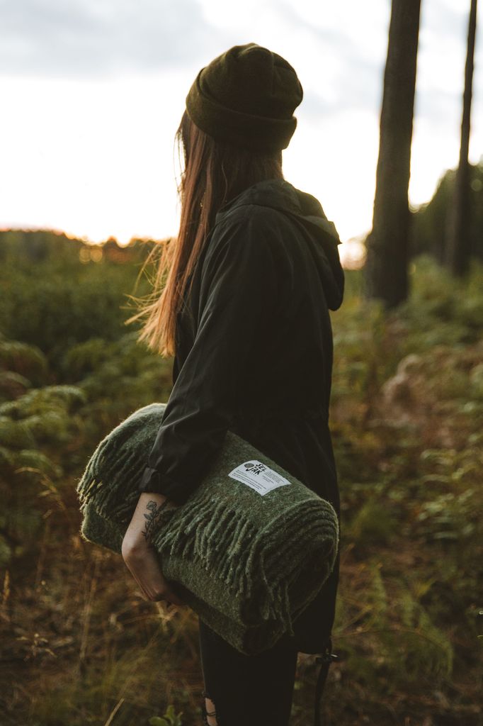 A woman holding a Moss Blanket - Fringe by Seljak Brand in the woods.