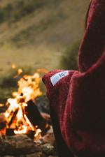 A woman sits by a campfire in a Pinot blanket from Seljak Brand.