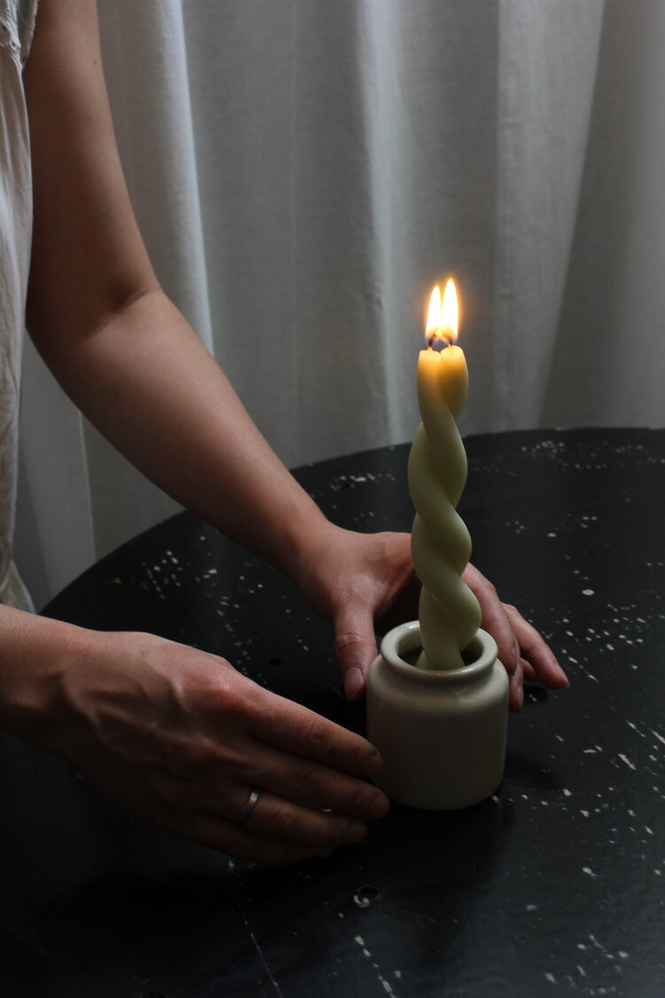 A person holding a Twisted Candle - Mother&#39;s Milk by Wax Atelier on a table.