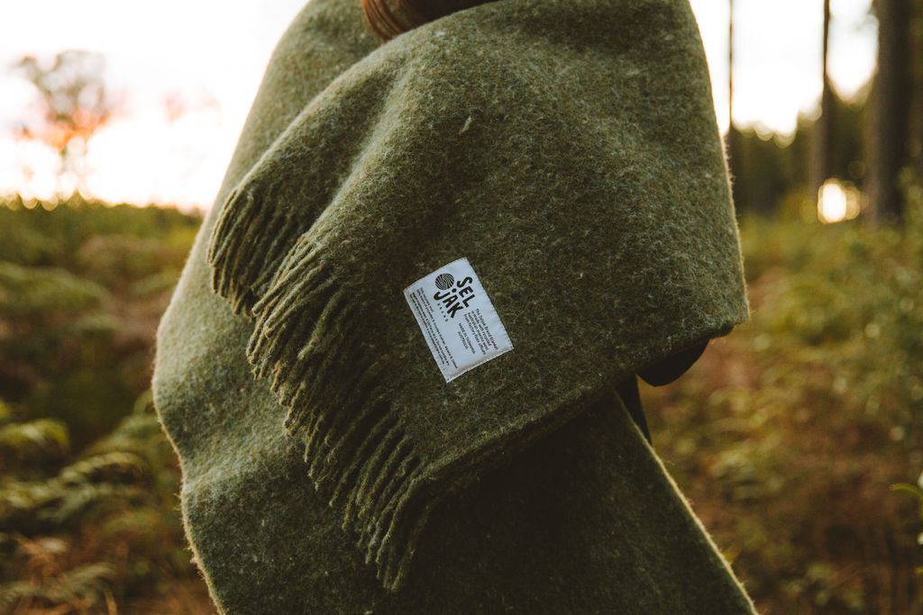 A woman wearing a Seljak Brand Moss Blanket – Fringe in the woods.