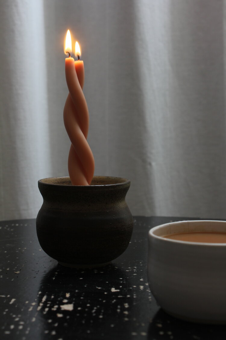 A Wax Atelier Twisted Candle - Pink Blossom sitting on a table next to a cup of coffee.