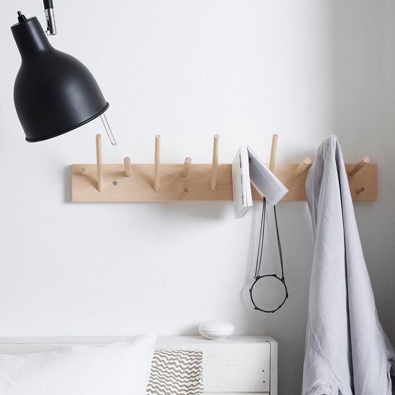 A versatile Iris Hantverk wooden multihanger shelf with hooks and an untreated lamp in a bedroom.