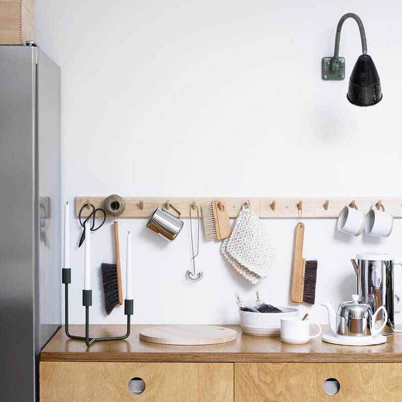 In this kitchen, a 7 Hook Peg Rail made of untreated birch from the brand Iris Hantverk is mounted on the wall. It serves as a functional and aesthetic shelf, holding various utensils.