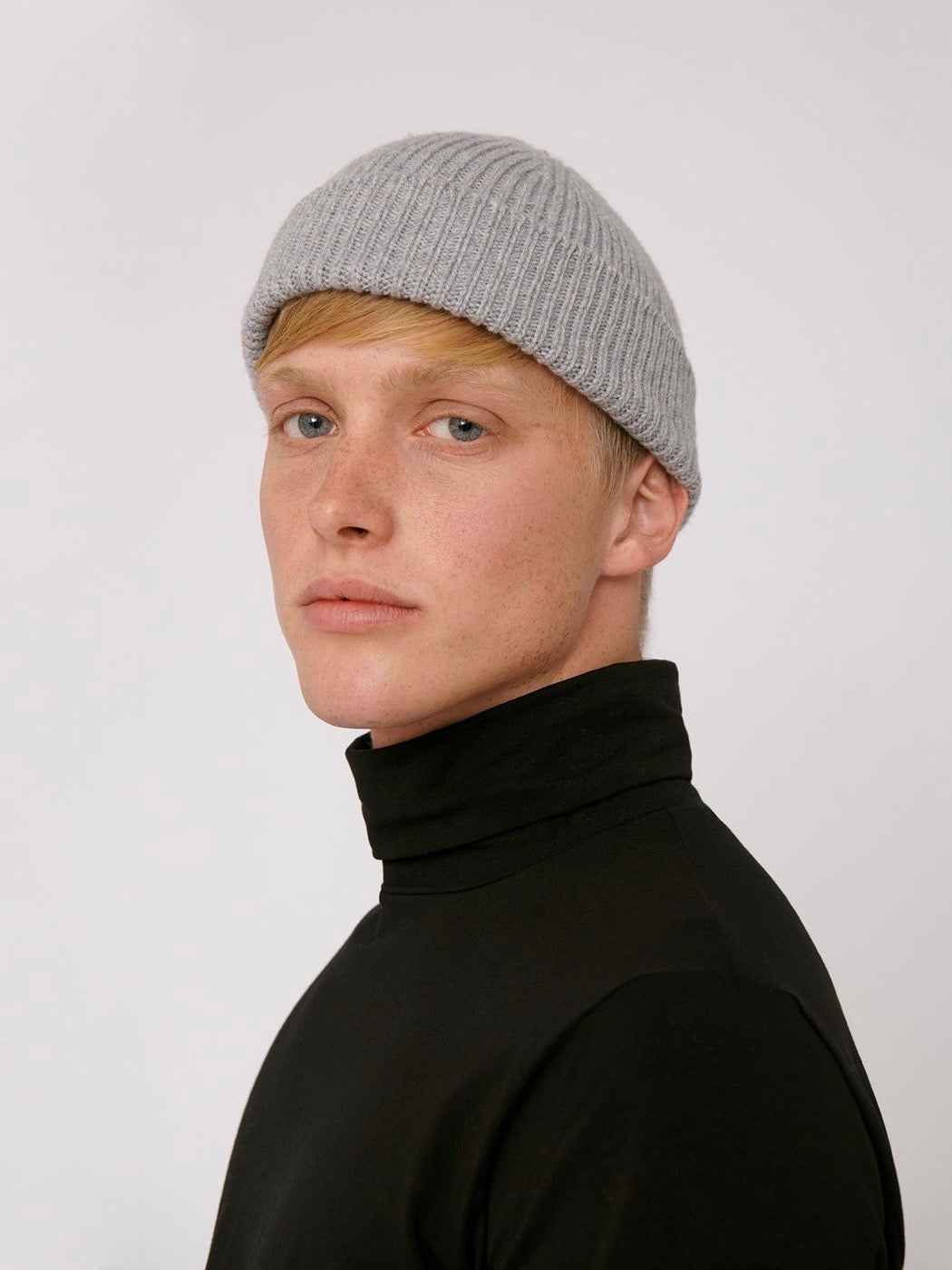 A man in a black turtleneck wearing an Organic Basics Recycled Cashmere Beanie - Grey.
