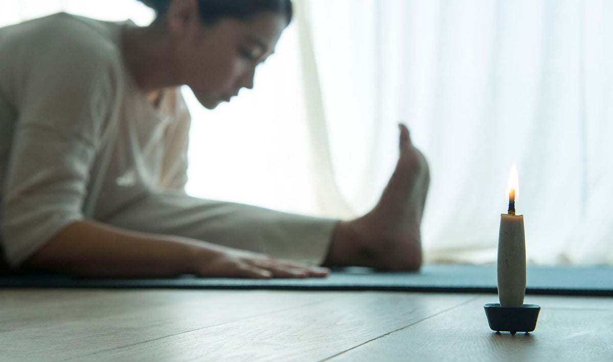 A woman is sitting on a yoga mat with a TOHAKU – Small (8 piece box set) candle from Takazawa in front of her.