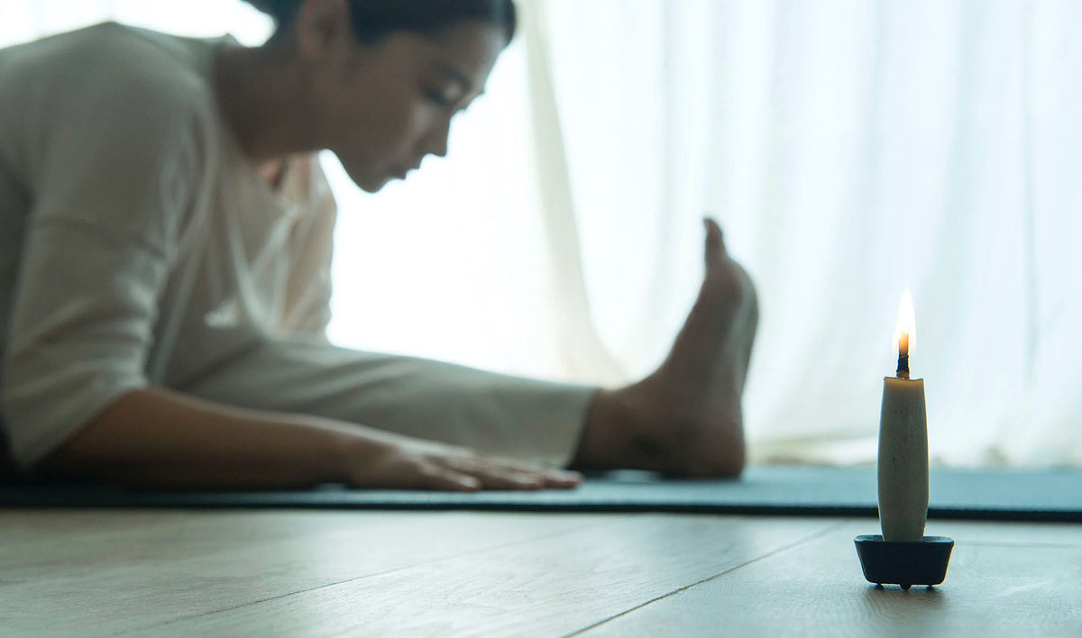 A woman is sitting on a yoga mat with a Takazawa Koma Iron Candle – Large in front of her.