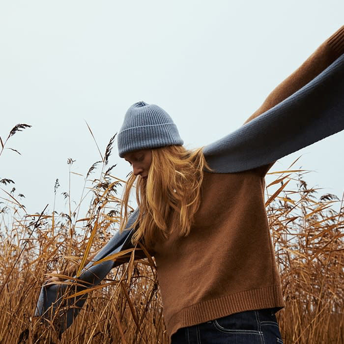 A woman standing in a field with her arms outstretched, wearing the Organic Basics Recycled Wool Beanie– Light Blue.