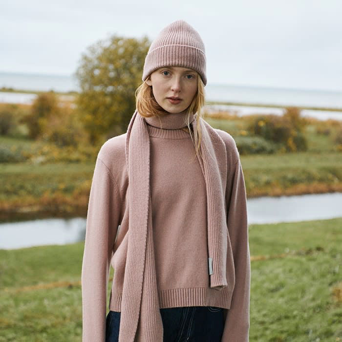 A young woman wearing an Organic Basics Recycled Wool Boxy Knit Jumper in Dusty Rose and a scarf.