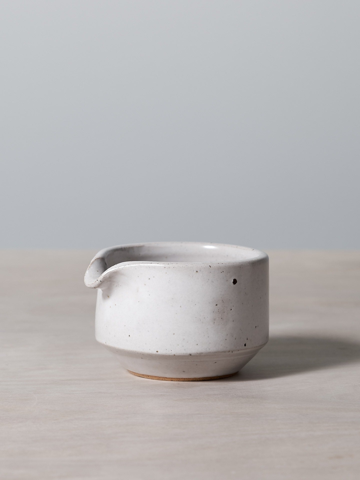 A small white Richard Beauchamp Straight Sided Creamer sitting on a wooden table.
