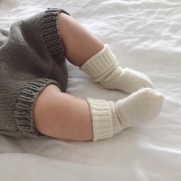 A baby is laying on a bed with Weebits Hand Knitted 2ply Merino Socks - Ivory on.