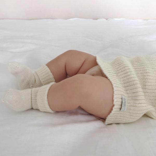 A baby laying on a bed wearing Weebits Hand Knitted 2ply Merino Socks - Ivory.