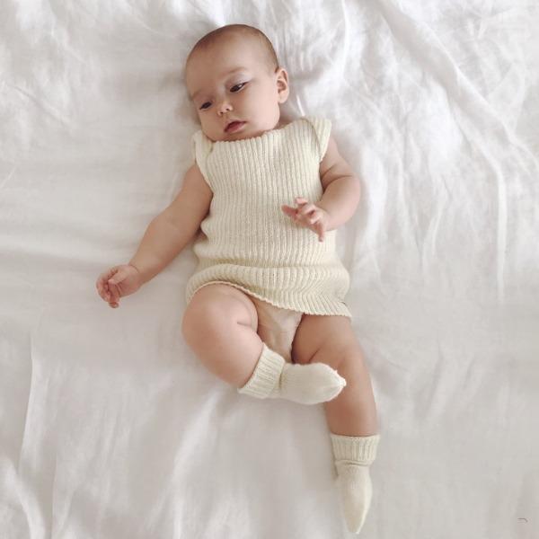 A baby is laying on a bed with Weebits Hand Knitted 4ply Merino Socks - Ivory on.