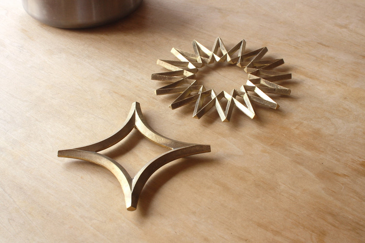 A pair of Galaxy Trivet – Solid Brass star shaped coasters by Futagami on a wooden table.