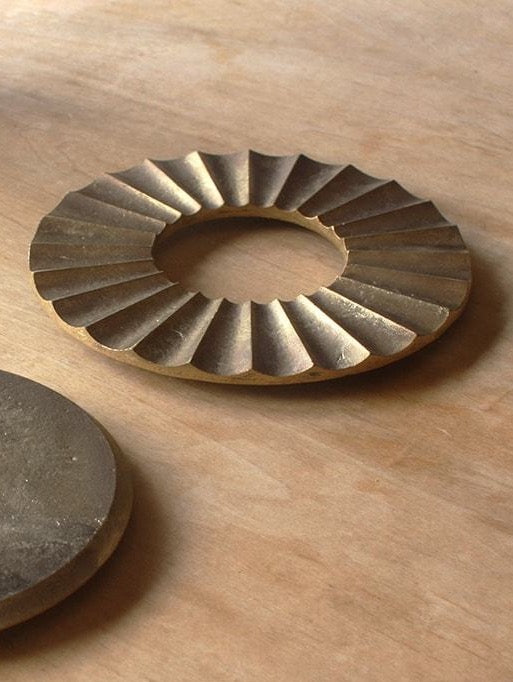 A pair of Sun Trivet – Solid Brass discs on a wooden table by Futagami.