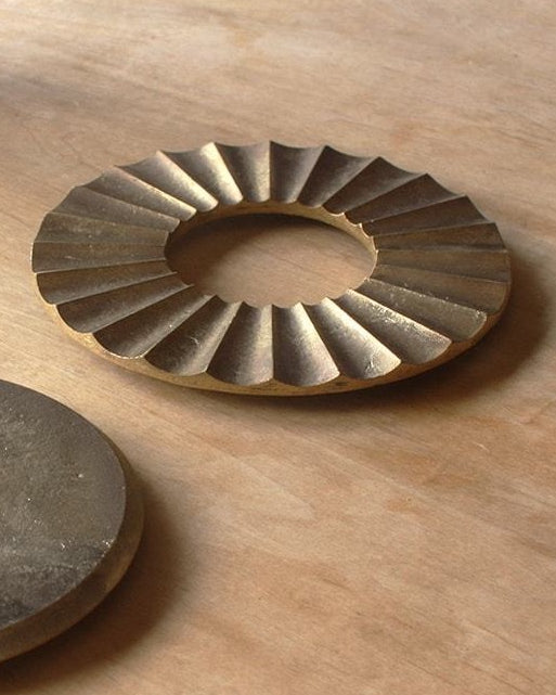 A pair of Sun Trivet – Solid Brass discs on a wooden table by Futagami.
